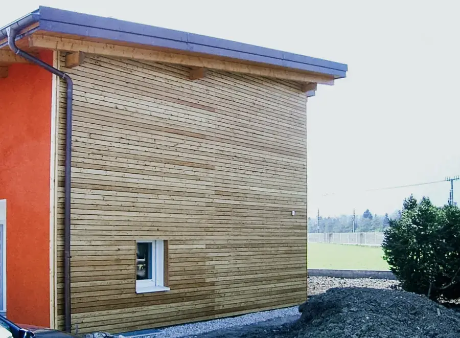 Rotes Wohnhaus mit seitlich angebrachter Holzfassade in Queroptik von RM Holzbau